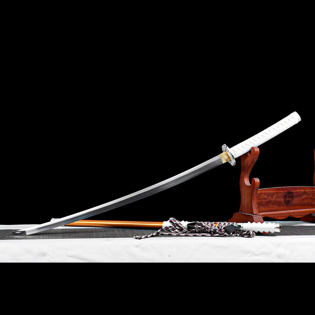 Battle ready curved spring steel tachi sword blade unsheathed next to orange scabbard