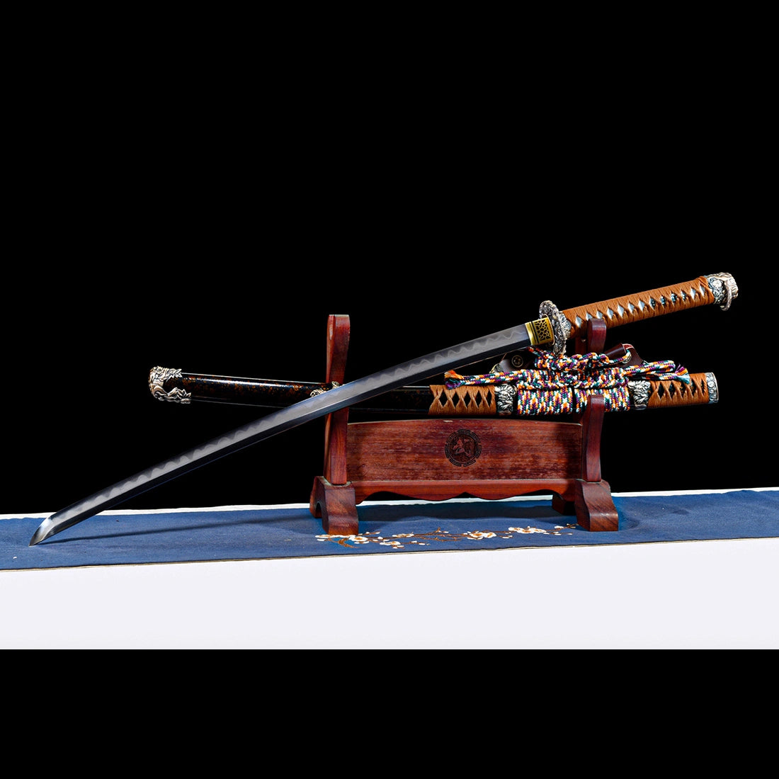 Dragonheir clay-tempered Damascus Tachi blade resting on wooden display stand with sheath and silk sageo below