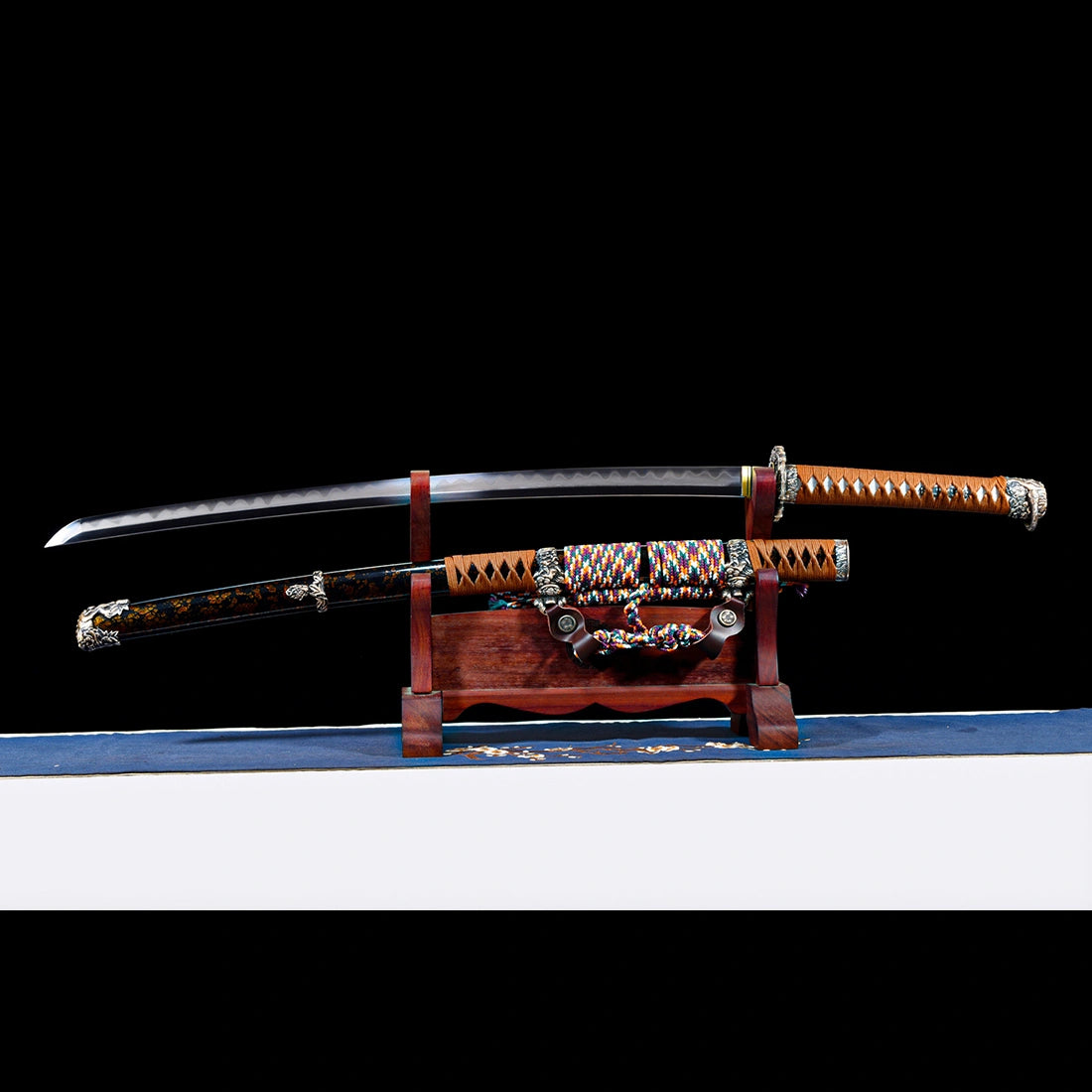 Dragonheir clay-tempered Damascus Tachi blade displayed horizontally above its gold-flecked lacquered Saya on dark stand