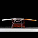 Hand-forged japanese tachi sword in orange lacquered scabbard resting on wooden stand