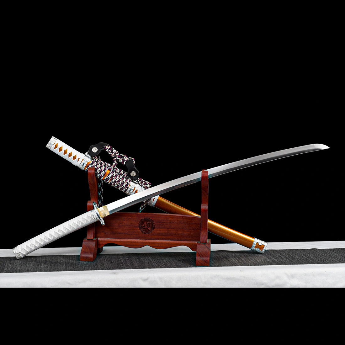Japanese tachi sword blade crossed with orange lacquered wooden scabbard on display stand