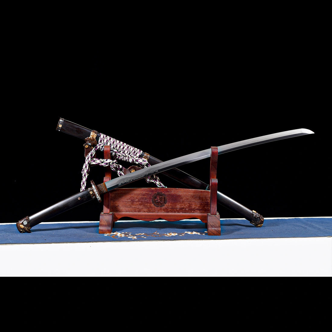 Unsheathed Tyrantclaw Wootz steel Tachi blade crossed over Brazilian ebony Saya scabbard on wooden display stand