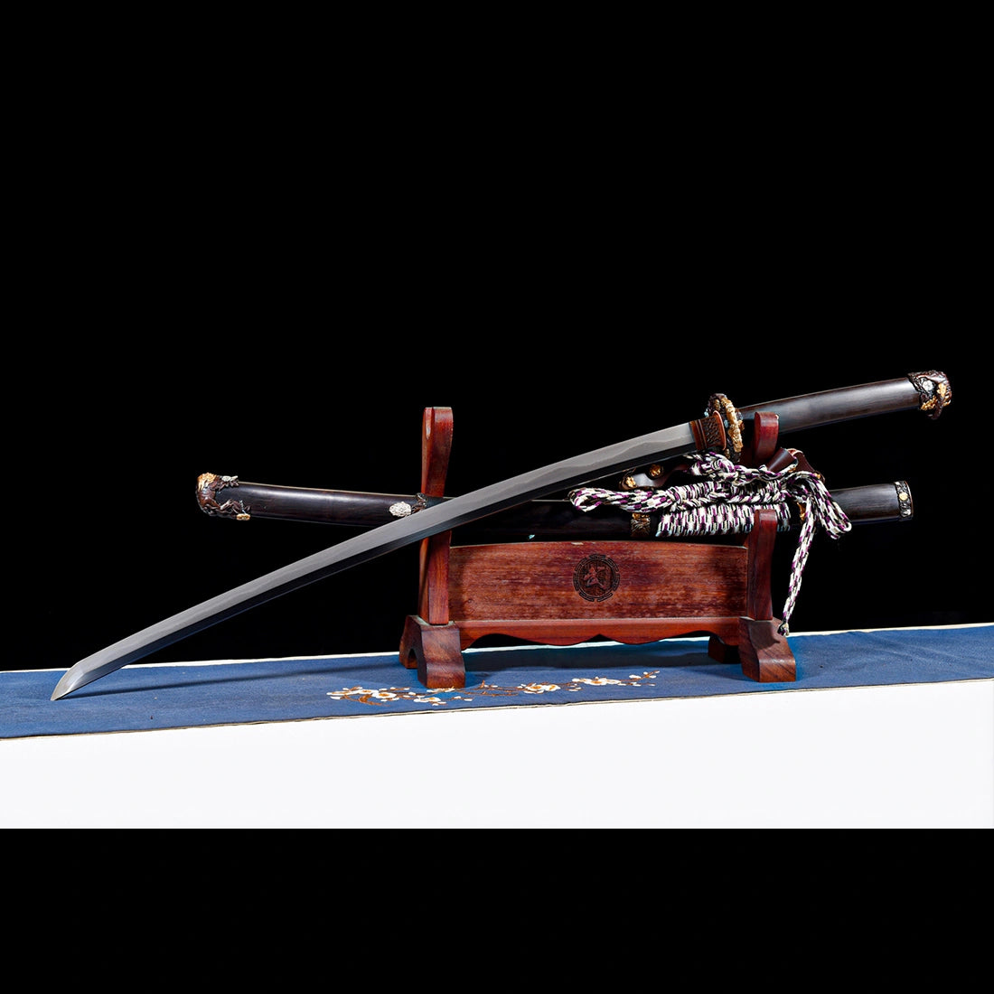 Full view of unsheathed Tyrantclaw Wootz steel Tachi sword resting on wooden display stand with Brazilian ebony Saya